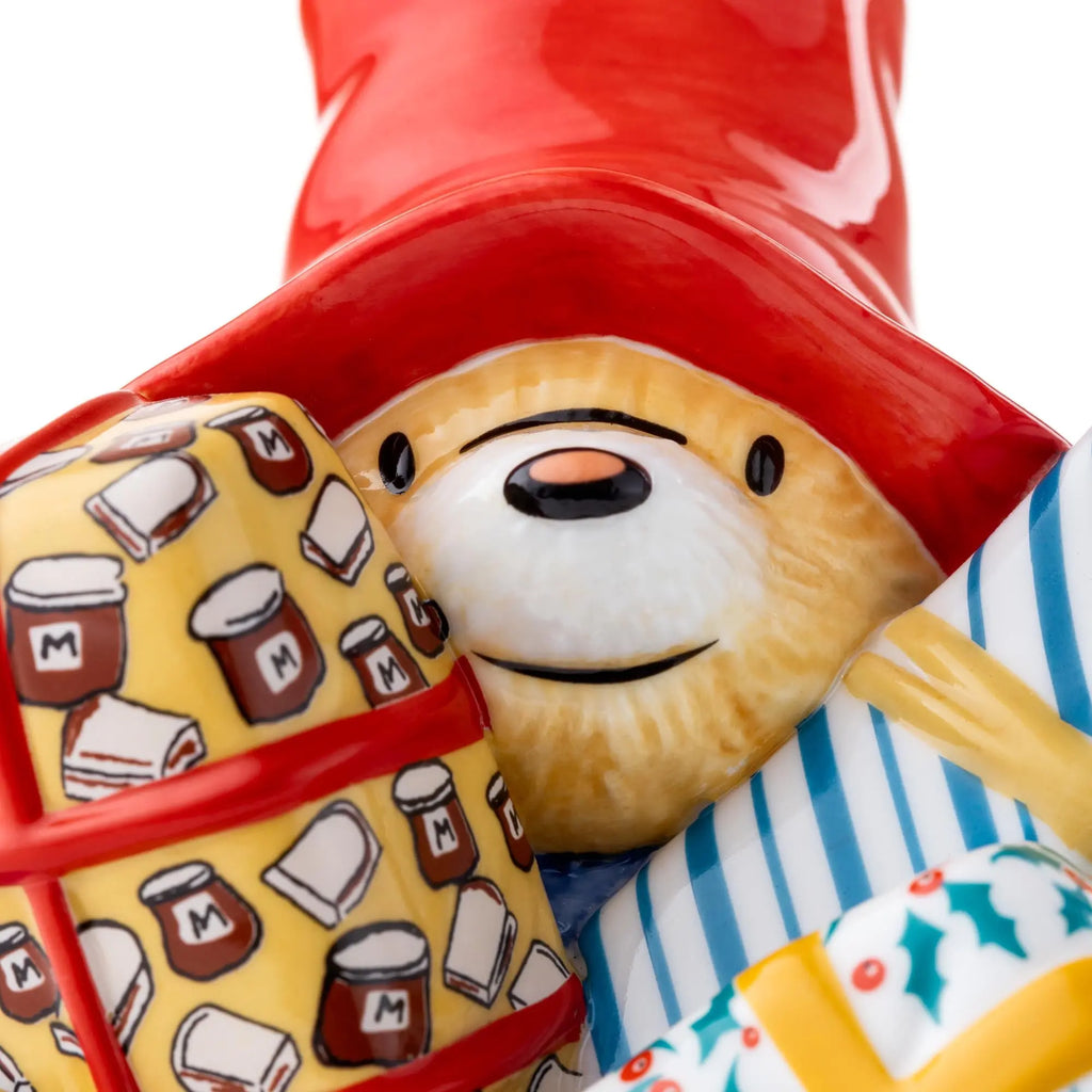 Close-up fine bone china figurine: bear head with red hat, patterned satchel and striped bag.